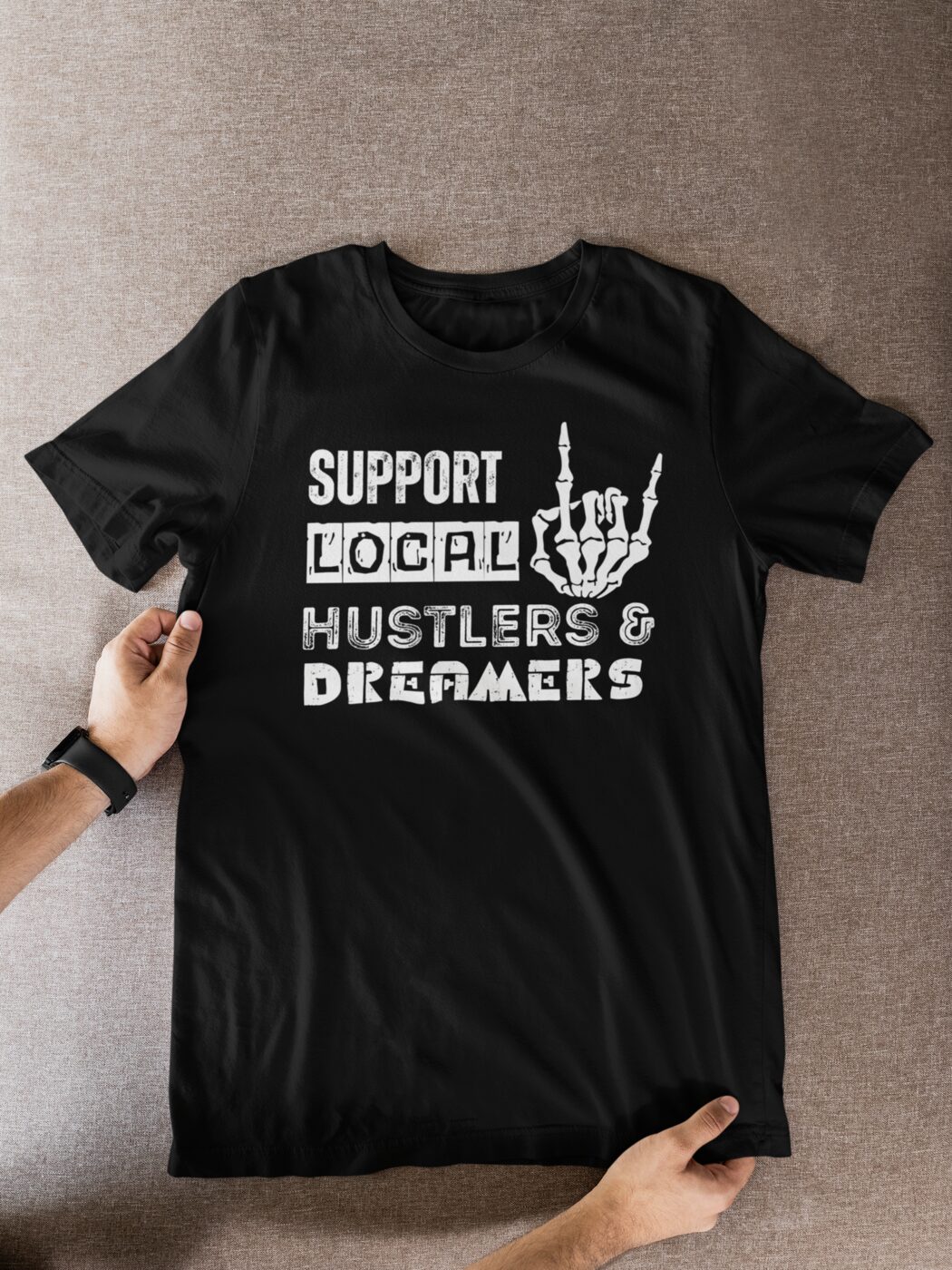 A black t-shirt held open reading Support Local Hustlers and Dreamers in white print.